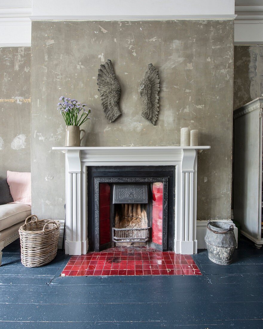 Artwork on wall above open fireplace with red tiles set in slate grey wooden floor; patinated walls