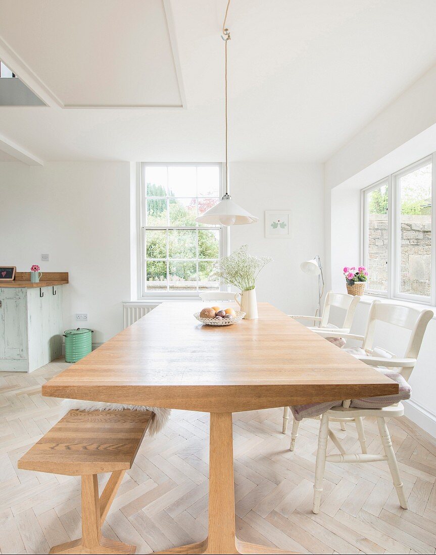 Dining table, bench and white chairs in open-plan light-flooded kitchen-dining room