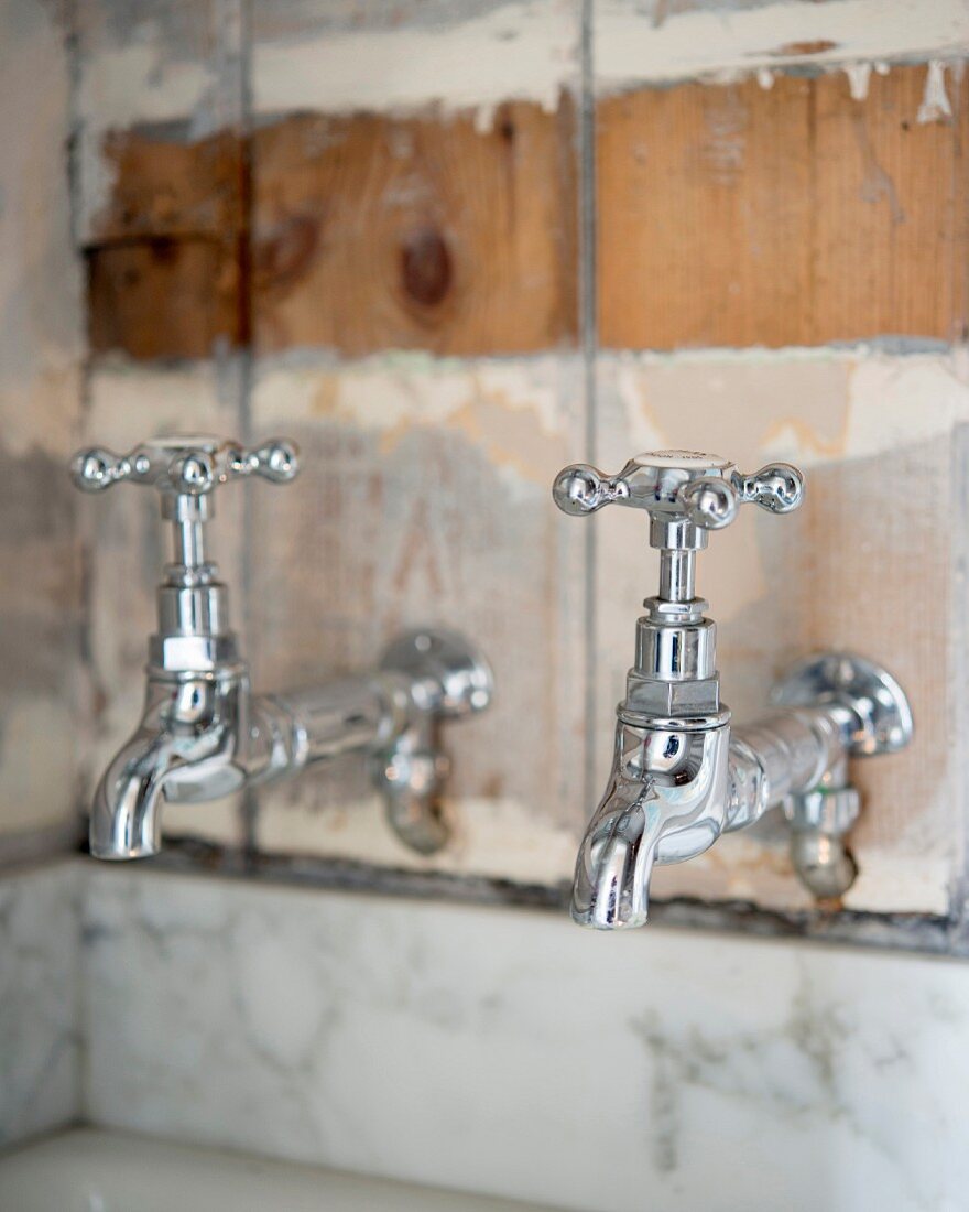 Retro-style taps mounted on patinated board wall above strip of marble cladding