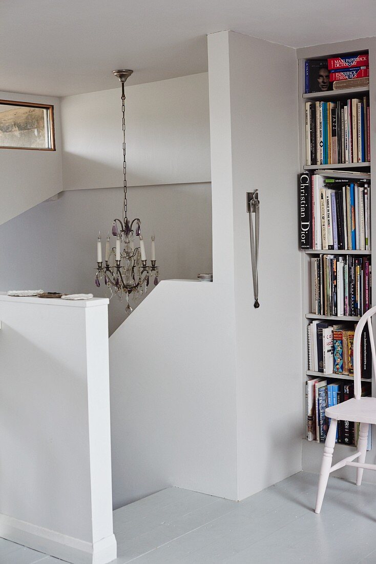 Head of staircase with white, solid balustrade and bookcase to one side
