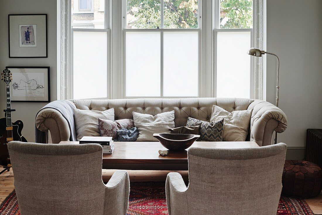 Traditionelle Couchgarnitur mit naturfarbenem Bezug und Retro Stehleuchte aus Chrom vor Fenster
