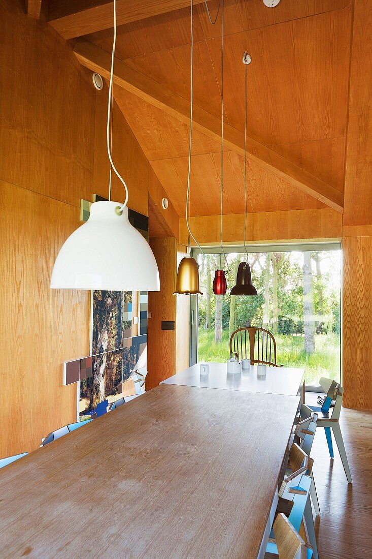 Two dining table pushed together below various pendant lamps in wood-panelled dining room