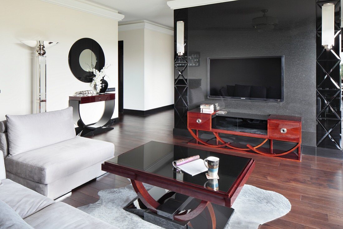 Eleganter Wohnraum mit Art Déco Möbel, hellgraue Polstergarnitur um Couchtisch, im Hintergrund Sideboard aus Mahagoniholz vor dunkelgrauem Raumteiler