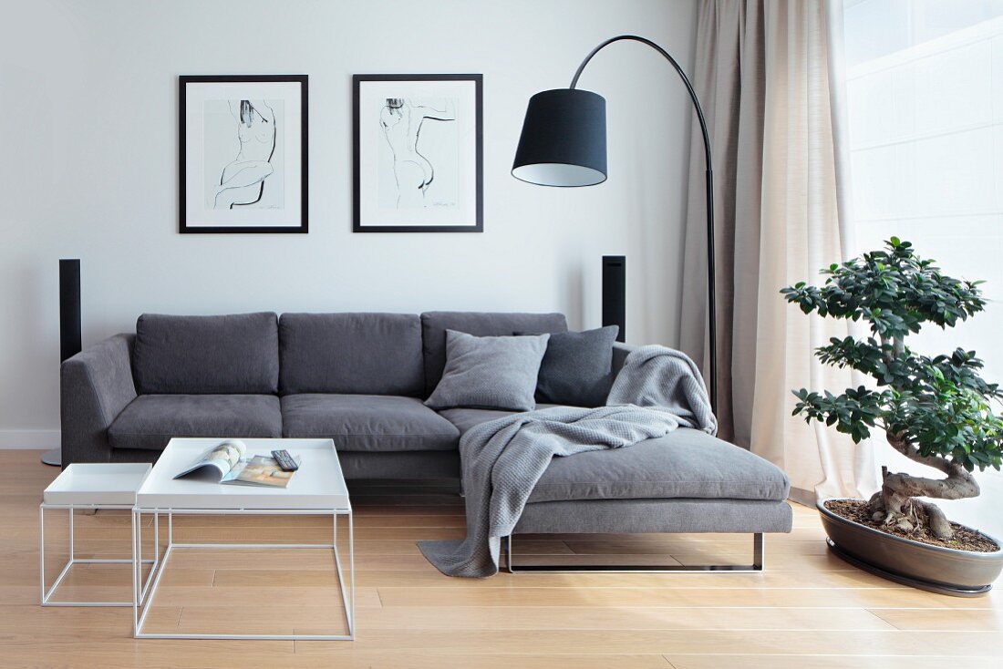 Couchtisch-Set in Weiß vor grauer Sofakombination, schwarze Bogenlampe und Bonsai Bäumchen am Fenster