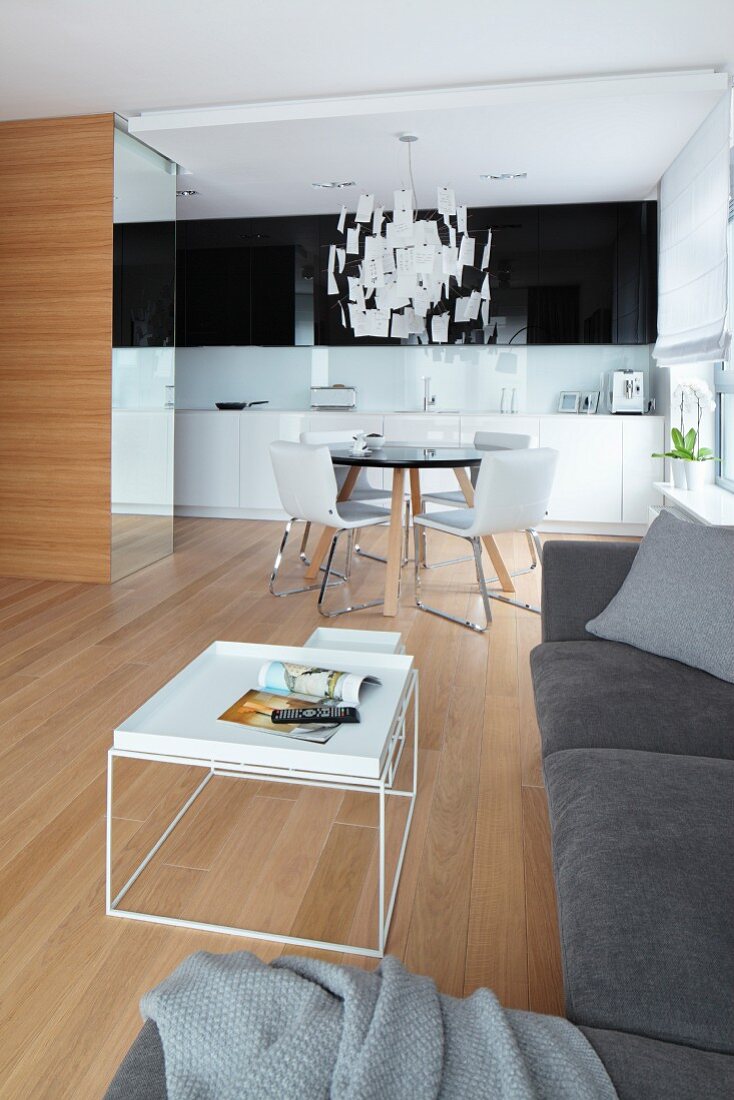 Nest of white coffee tables, grey sofa combination and dining area in background in open-plan kitchen