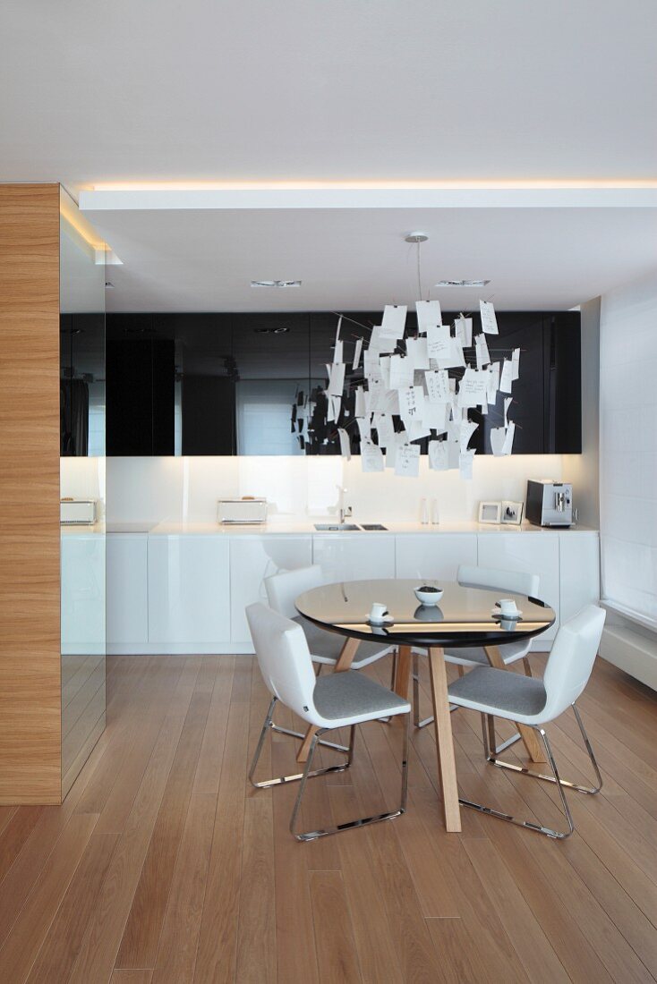 Esstisch mit schwarzer, runder Platte und weiße Stühle unter Designer-Zetteleuchte in offener Küche
