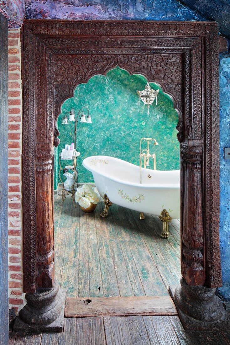 View through doorway with carved wooden surround of free-standing vintage bathtub against green wall