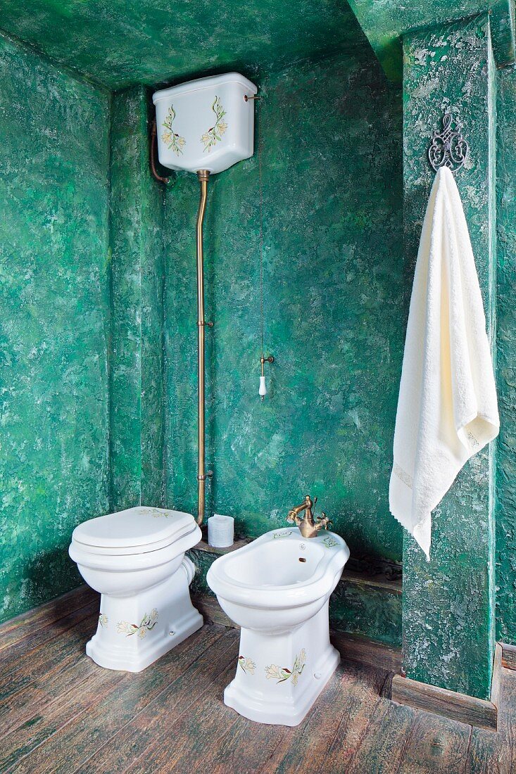 Toiler with cistern and bidet against green, sponged wall in rustic bathroom