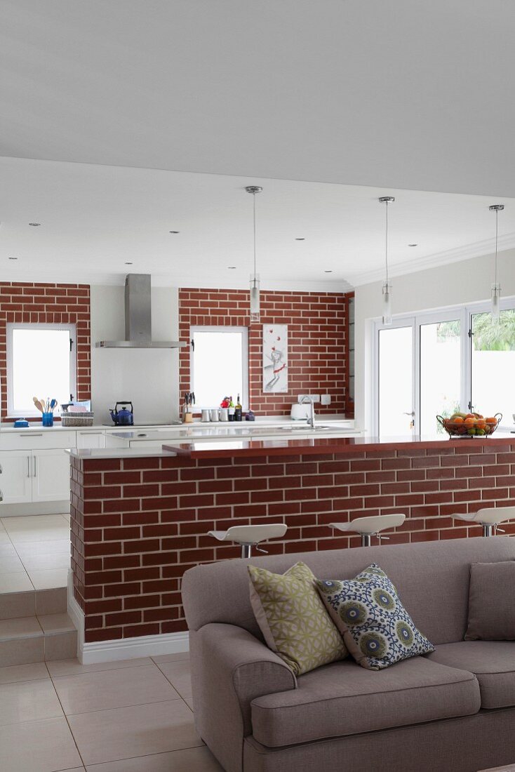 Sofa in open-plan living area in front of brick counter and kitchen counter against brick wall in background