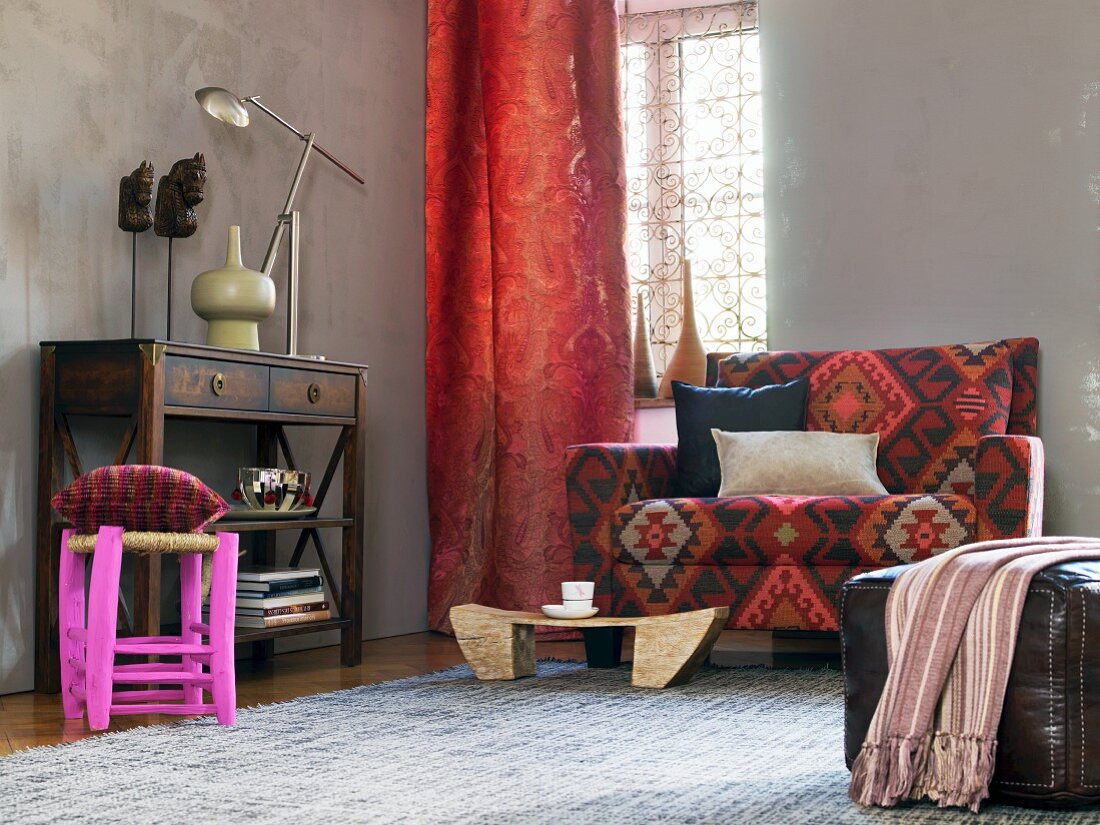 African-style living area - sideboard, red curtains, patterned sofa and leather pouffe