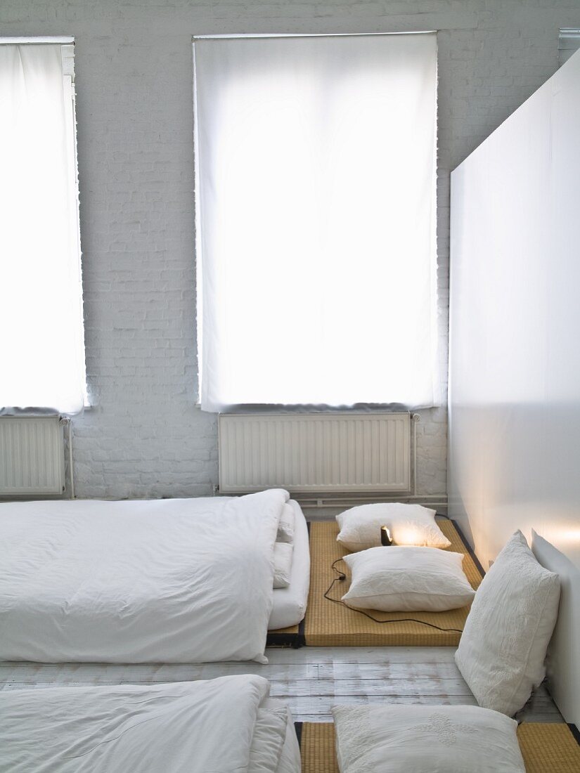 Japanese-style sleeping area with white curtains on windows and whitewashed brick wall