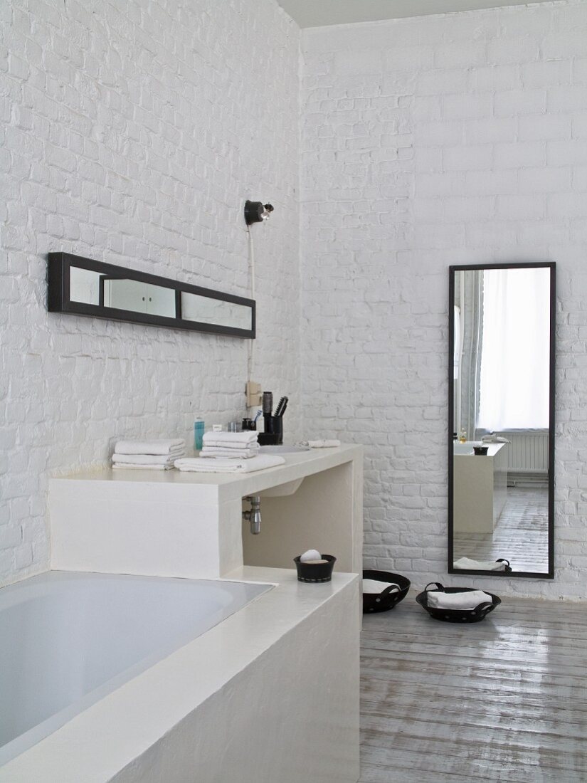 Eingebaute Badewanne und gemauerter Waschtisch vor geweisselter Ziegelwand, im Hintergrund Wandspiegel