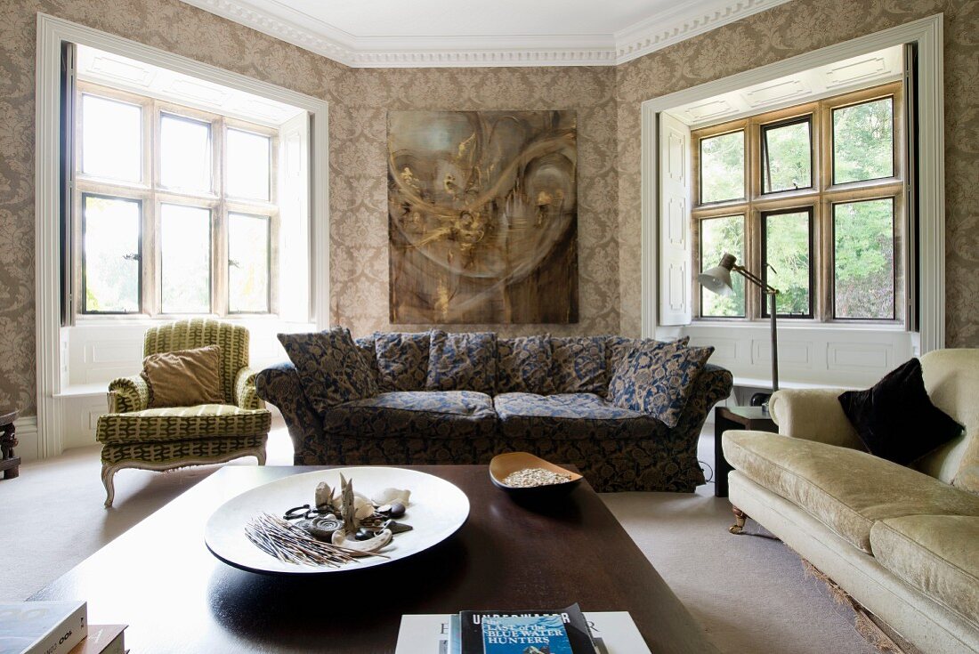 Blick über Couchtisch auf gemustertes Polstersofa, seitlich Rokoko Sessel in polygonalem Wohnzimmer