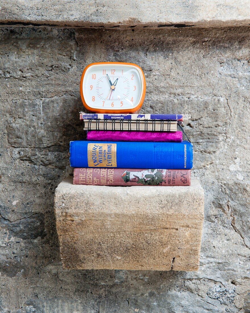 Wecker und Bücherstapel auf Vintage Steinkonsole an Natursteinwand