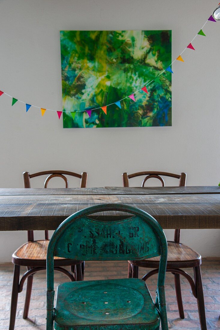 Vintage metal chair and Thonet chairs at wooden dining table in front of bunting and artwork on wall