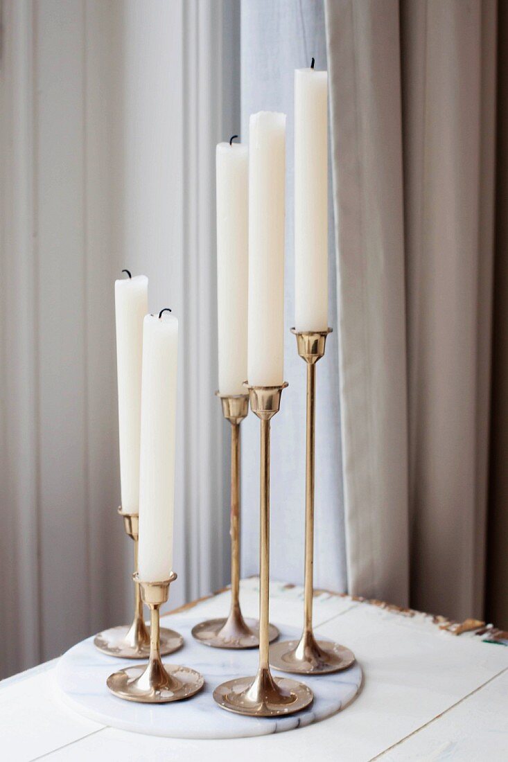 Five white candles with extinguished wicks in bronze candlesticks on marble board
