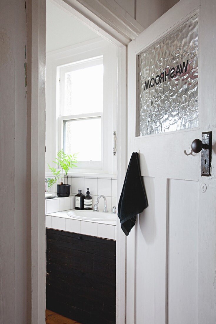 Blick durch offene Altbau Badezimmertür auf gefliesten Waschtisch mit schwarzem Schubladenunterbau