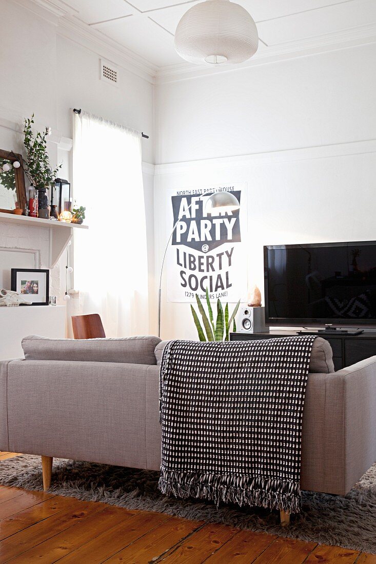 Sofa mit schwarz-weiss gemusterter Fransendecke und politischem Plakat neben Fernseher