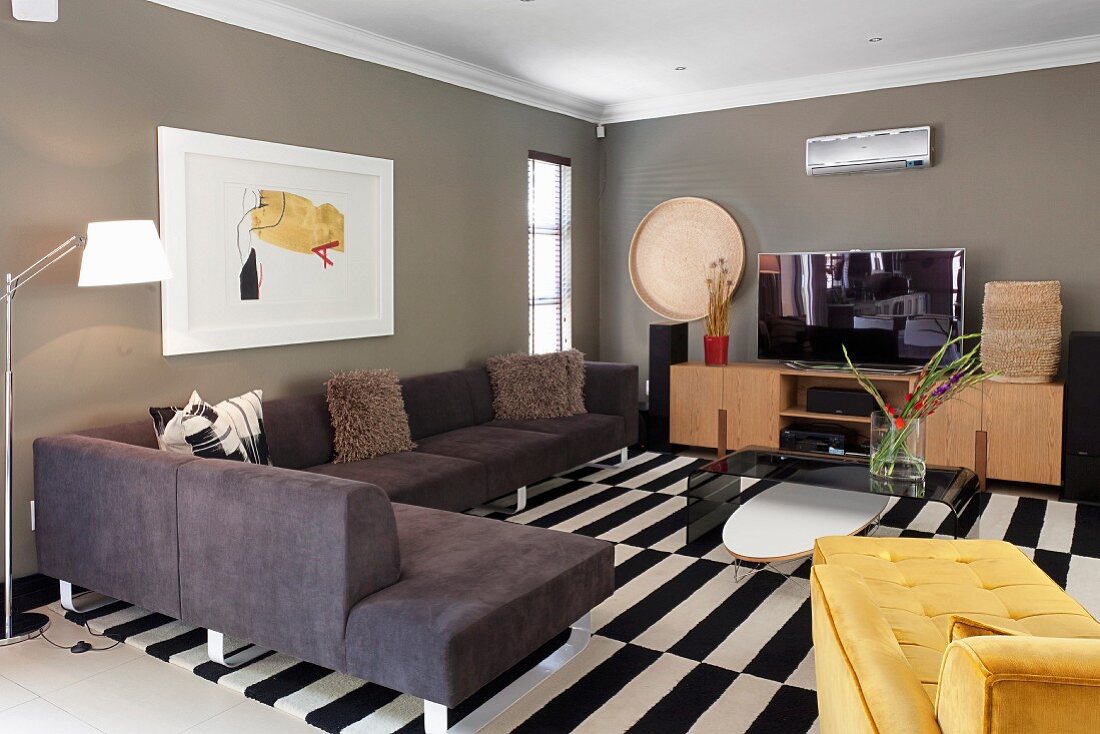 Moderne Polstercouch übereck und gelbe Tagesliege auf schwarz-weißem Teppich in Wohnzimmer, mit grau getönten Wänden