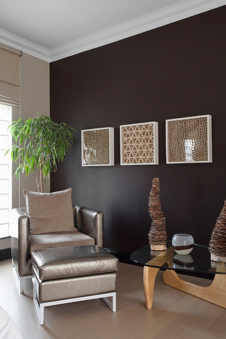 Sessel und Fussschemel mit silberfarbenem, glänzendem Bezug und Klassiker Coffeetable vor dunkelbraun getönter Wand, mit weiss gerahmten Glaskästen