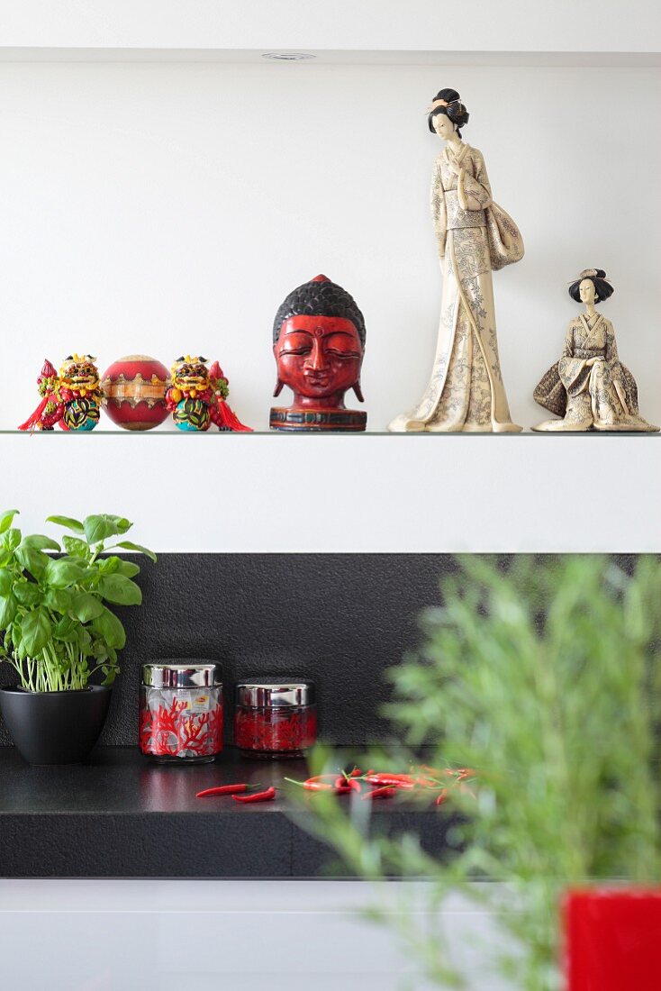 Oriental ceramic figurines and head of Buddha on white shelf