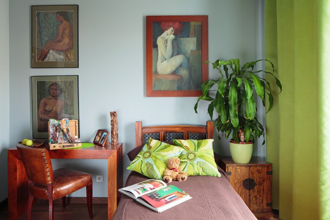 Bett zwischen Arbeitsplatz und Beistelltisch mit Grünpflanze, an Wand Bildersammlung mit Frauenmotiv