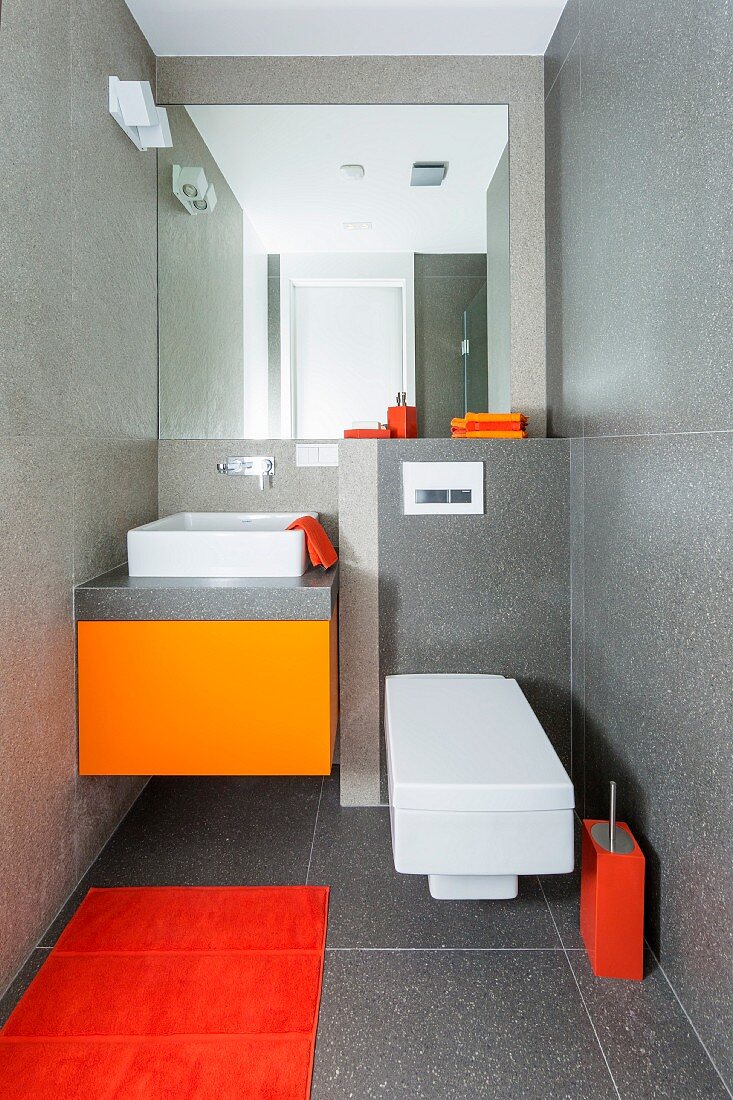 Gäste-WC in Designerstil mit grau gefliesten Wänden und Farbakzenten in Orangetönen