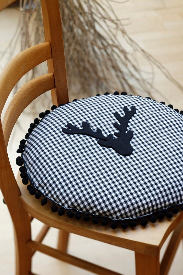 Round cushion made from blue and white gingham cotton decorated with pompom trim and stag's head appliqué