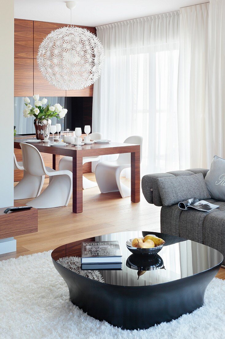 Schwarz glänzender Coffeetable auf Hochflorteppich und Designerleuchte über Esstisch mit weissen Panton-Stühlen