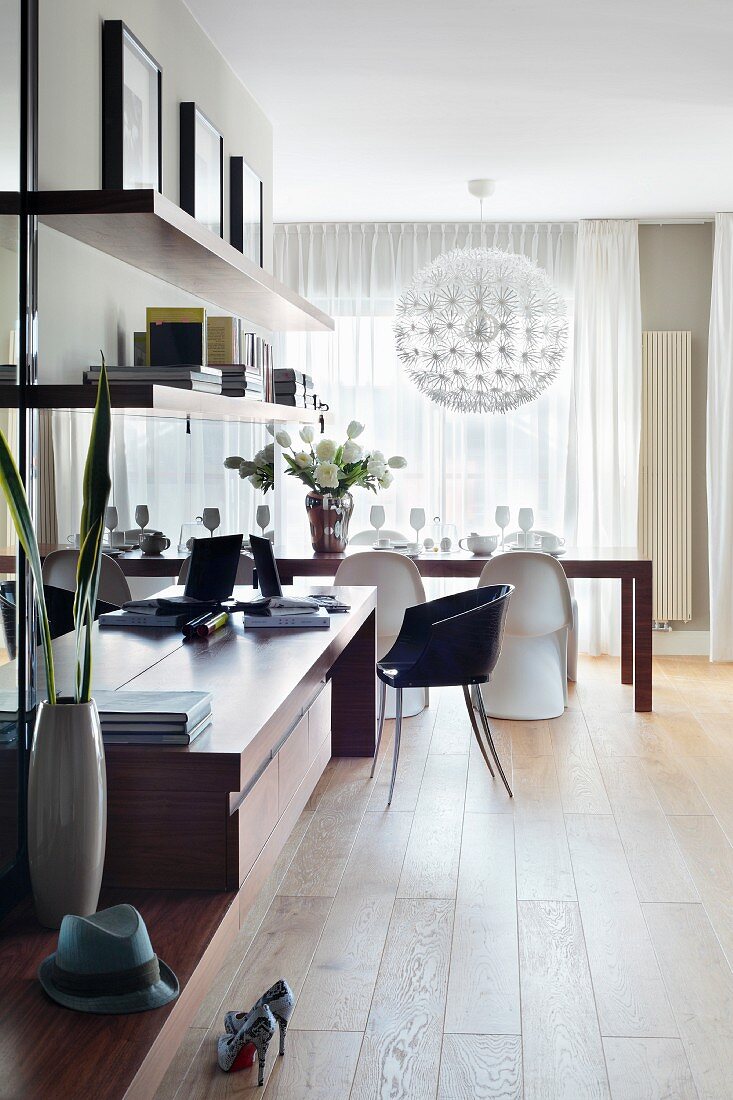 Sideboard with workspace and bookshelves in open-plan interior with classic chairs at dining table in background
