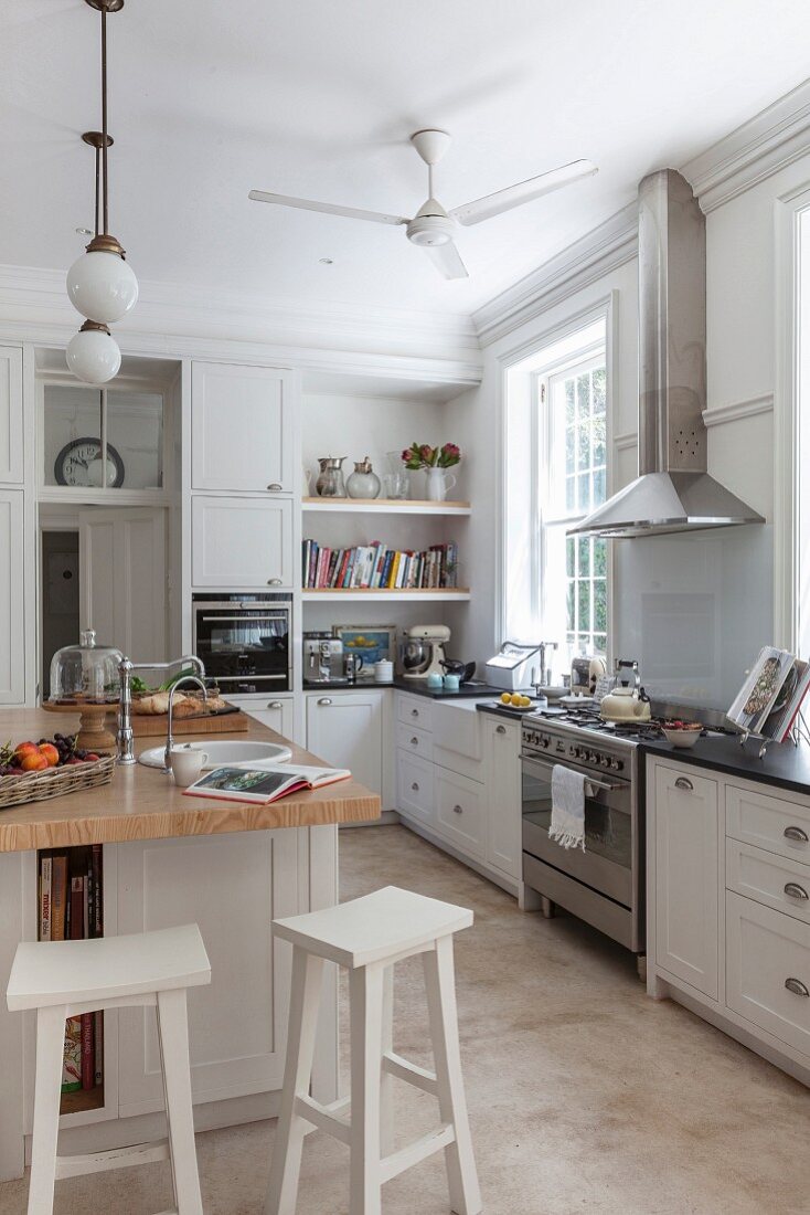 Modern country-house kitchen with white cupboards and free-standing central counter with white-painted bar stools