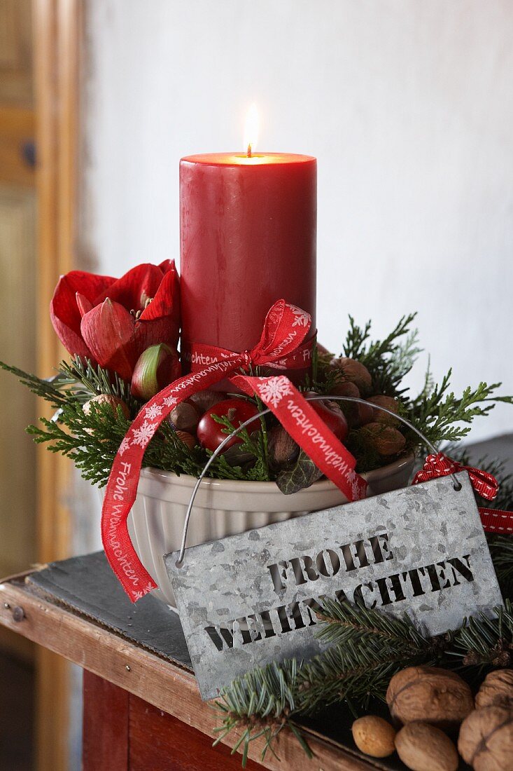 Festive arrangement with lit candle in ceramic bowl with Christmas greetings on zinc sign and ribbon