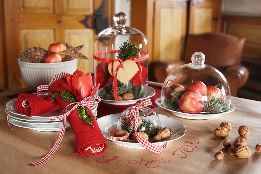 Plates of nuts, apples and pine cones under glass covers on festive table