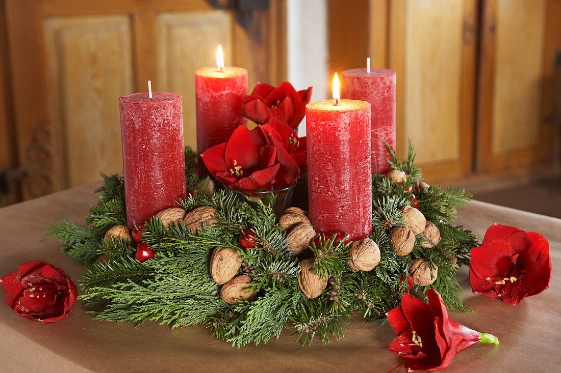 Klassischer Adventskranz mit Tannengrün und Thuja-Zweigen, Walnüssen, Amaryllisblüten und roten Kerzen