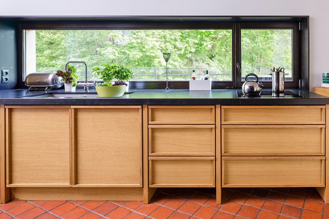 Moderne Küchenzeile mit Holzeinbauten unter schwarzer Platte, vor Fensterband mit Aussicht