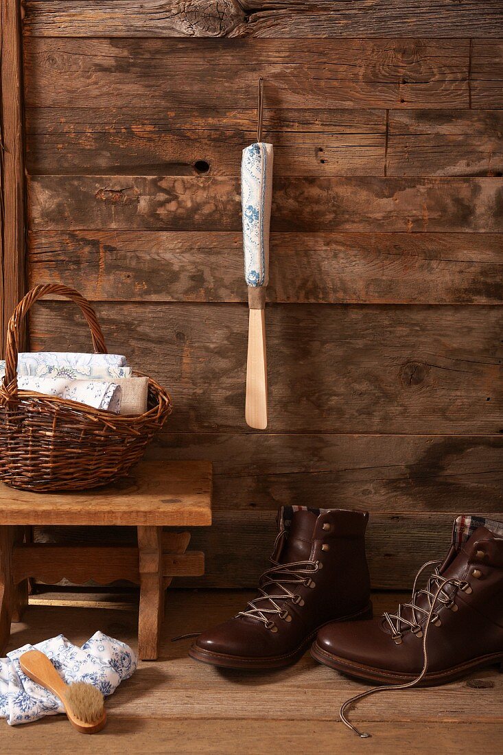 Schuhlöffel mit selbst gestaltetem Griff an Holzwand aufgehängt, davor Schnürschuhe und Schemel