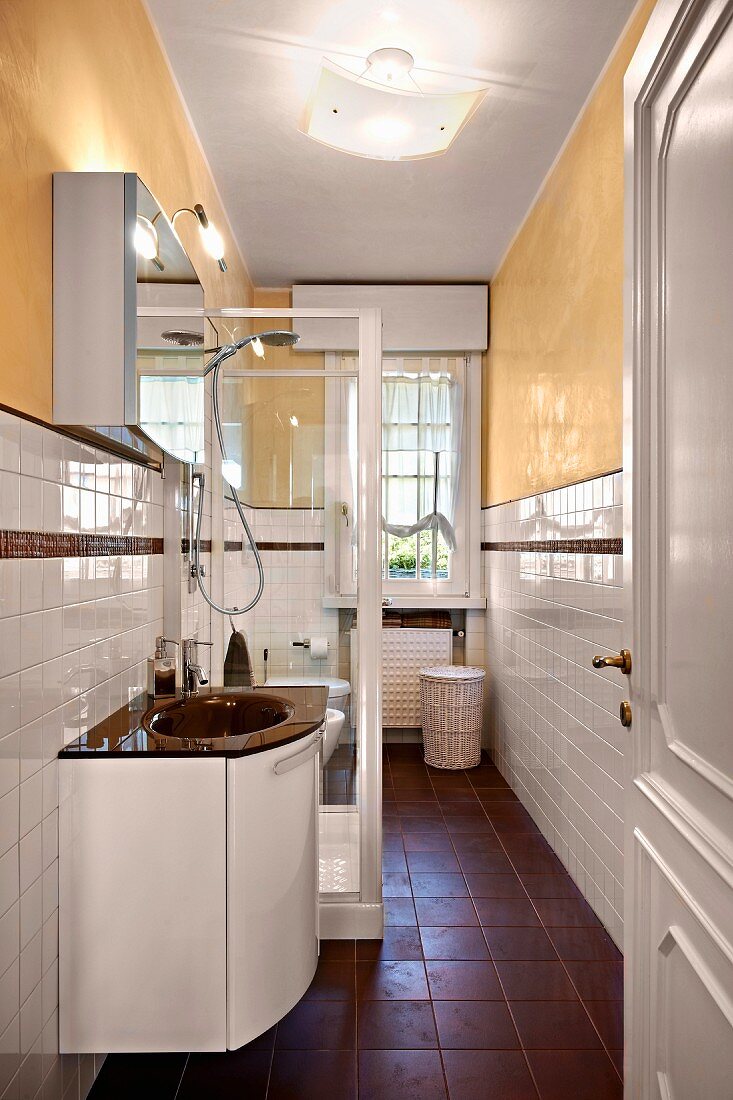 Waschtisch neben verglaster Duschkabine in schmalem Bad, Wände teilweise weiss gefliest und gelb gestrichen