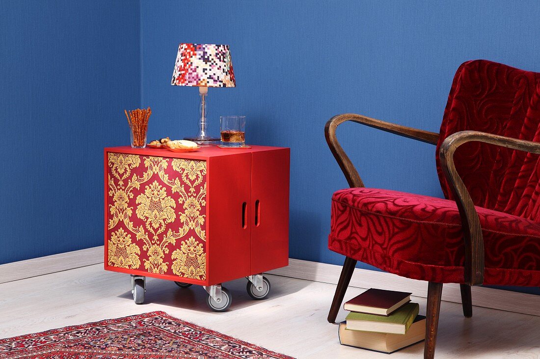 DIY minibar made from two wooden crates covered in wallpaper on castors next to 50s armchair