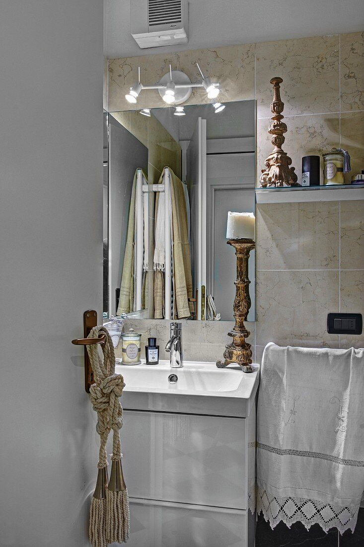 Antique candlestick on washstand below mirror on wall covered in sandy marble tiles