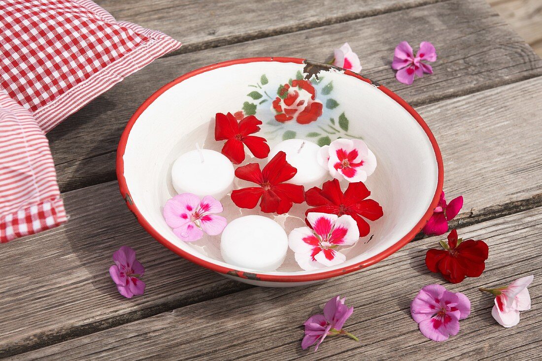 Geranienblüten und Schwimmkerzen in Vintage Emailleschüssel auf Holztisch