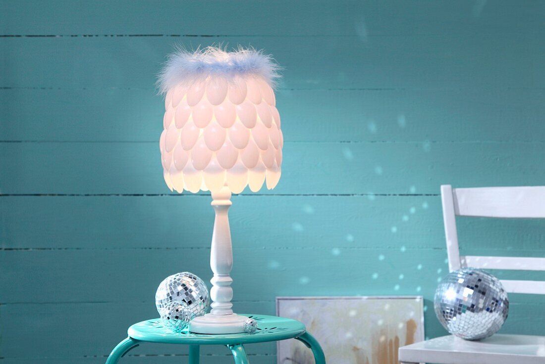 Lampshade hand-made from plastic spoons and feather trim in front of turquoise background