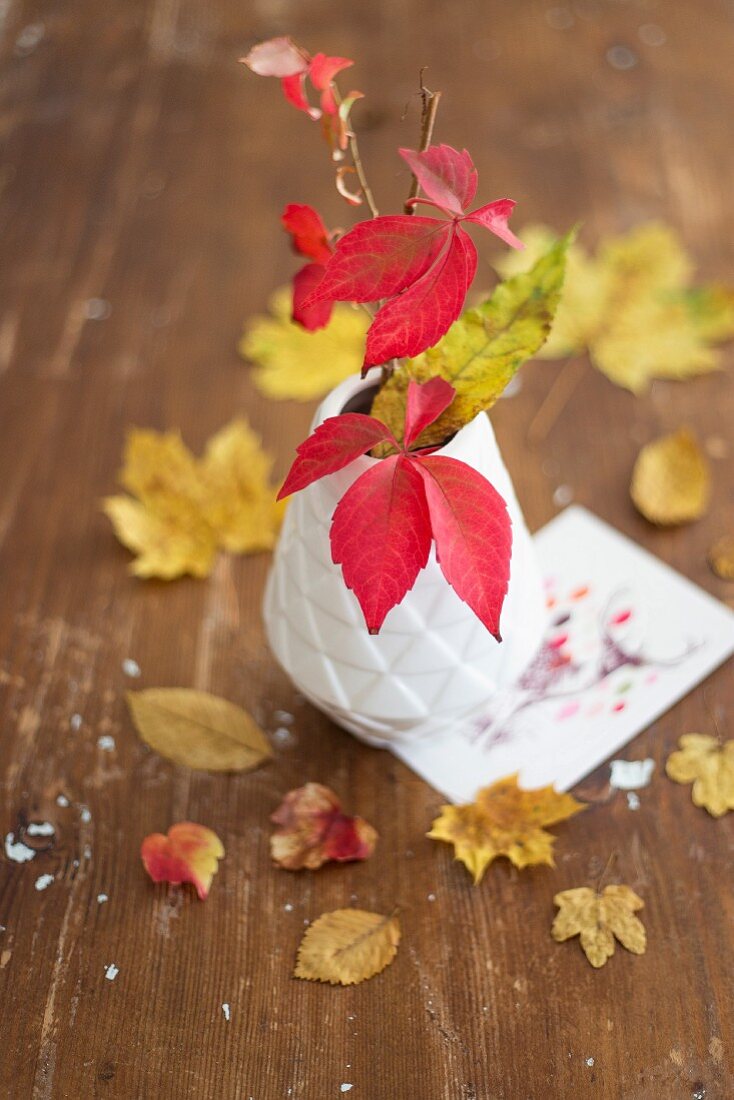 Autumnal table arrangement with yellow leaves and white vase of red leaves