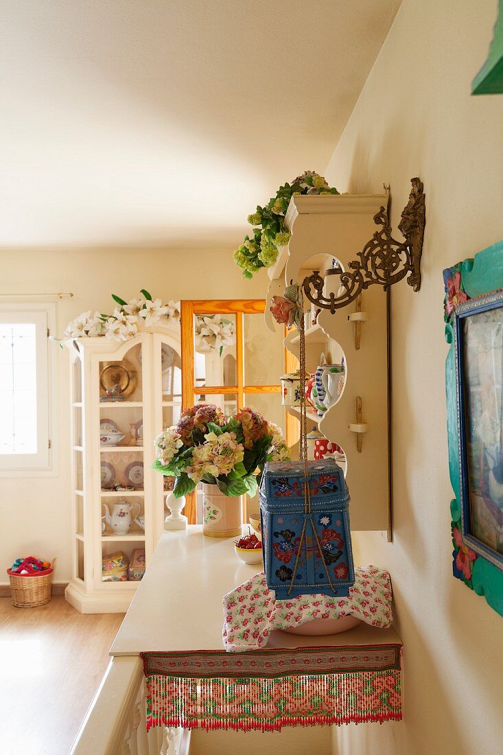 Mit Ablage überdeckter Treppenabgang, romantisches Tellerbord und Vitrine mit Blumenschmuck