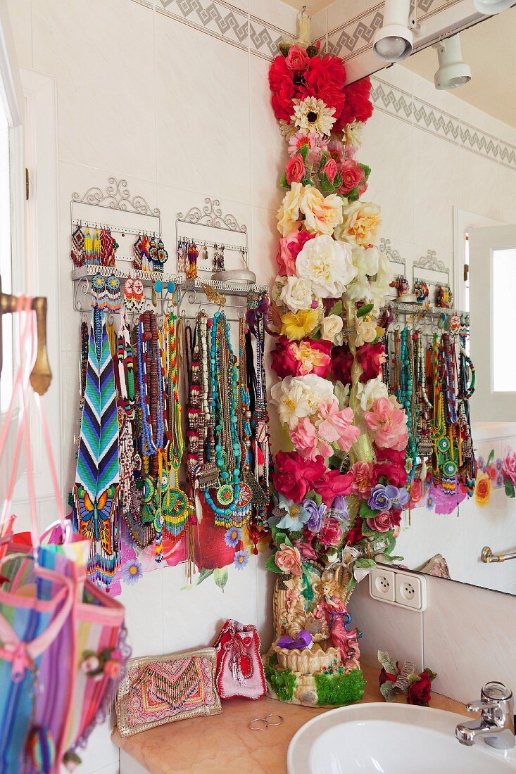 Sammlung von bunten Hippie-Ketten und eine Ranke aus Stoffblumen im Badezimmer