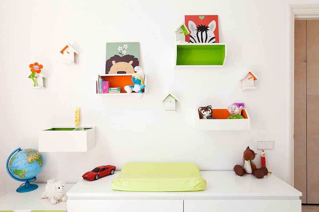 Kommode mit Wickelauflage vor weisser Wand, oberhalb aufgehängte Holzkästchen mit Spielzeug dekoriert