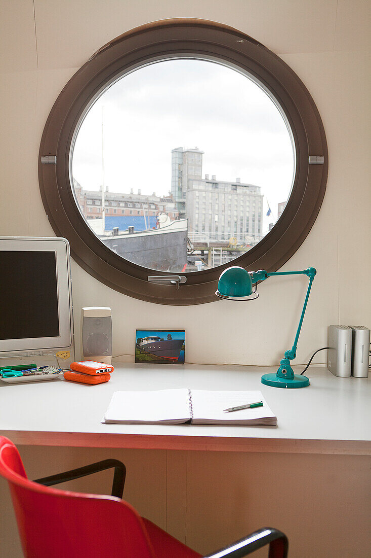 Schreibtisch mit Retro Tischlampe vor Bullaugenfenster mit Stadtblick