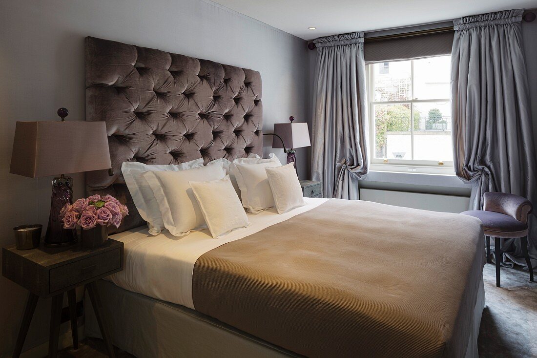 Bedroom with button-tufted headboard, bedside tables and floor-length grey curtains