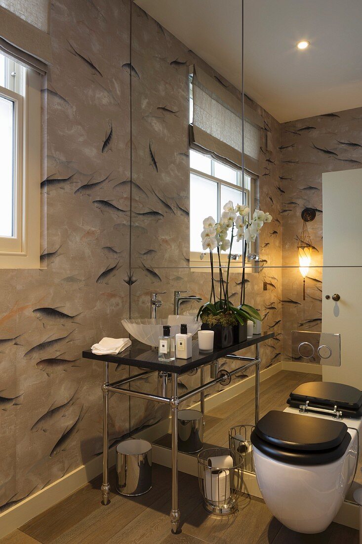 Toilette und eleganter Waschtisch mit Waschbecken in Muschelform vor Spiegelwand, an Wand Tapete mit Fischmotiven
