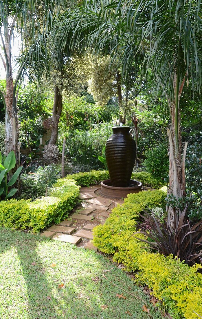 Exotic gardens with amphora-shaped fountain below palm trees
