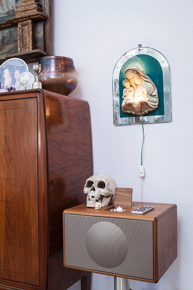 Totenschädel auf Retro Musikbox, vor Wand mit beleuchtetem Madonnenbild